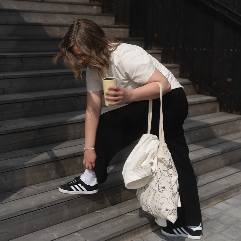 Anna Ahonen kumartuneena kenkiä kohti termosmuki toisessa kädessä. 